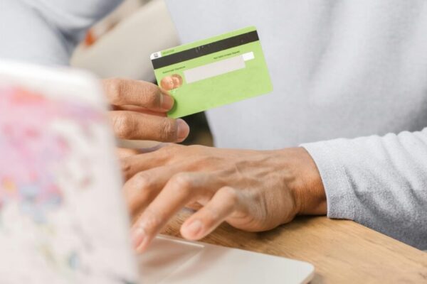Close-up of hands holding a green credit card for an online purchase using a laptop, depicting secure transactions.