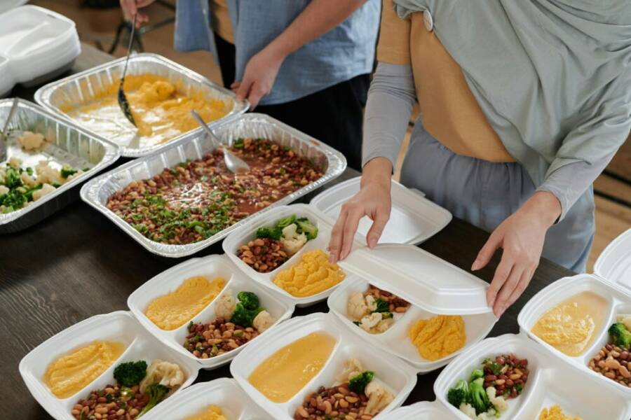 Preparing various lunch boxes with vegetables, beans, and hummus for meal distribution.