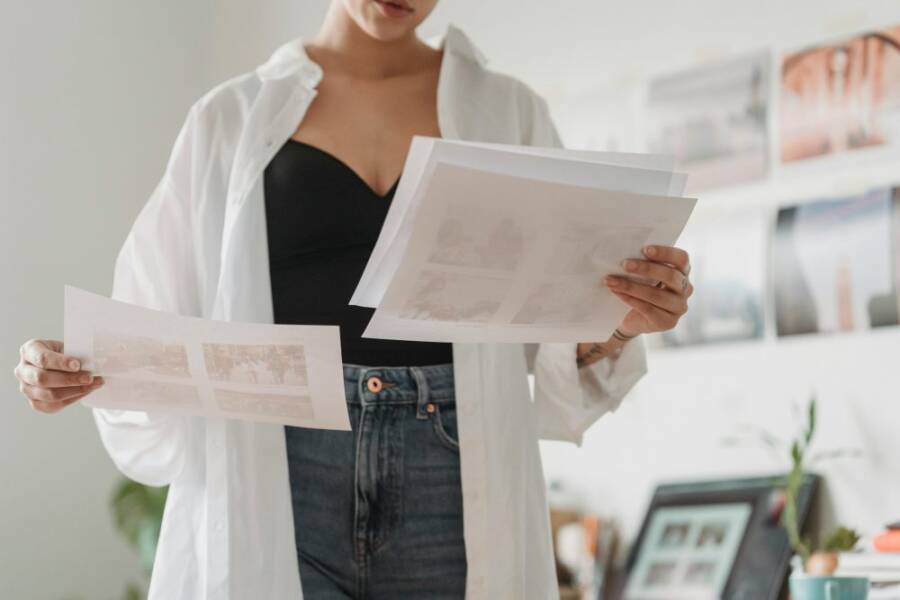 Woman in casual attire analyzing printed photos indoors with focus on creative work.