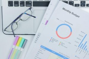 A clean office desk setup featuring a laptop, glasses, and a colorful budget report.