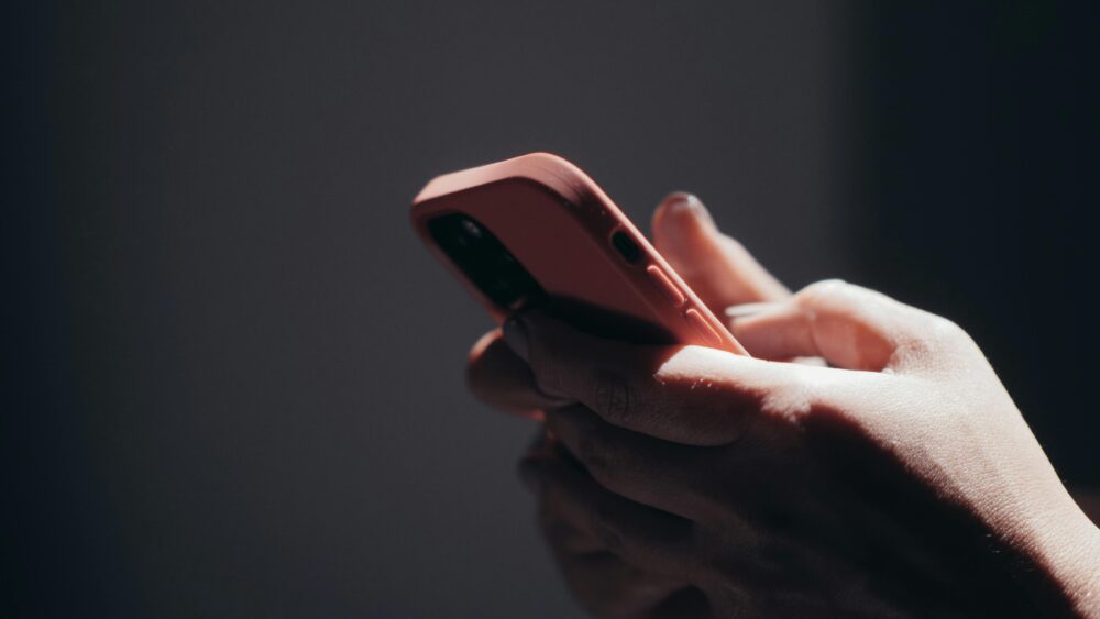 Close-up of hands holding a smartphone in dim lighting, showcasing texting or browsing activity