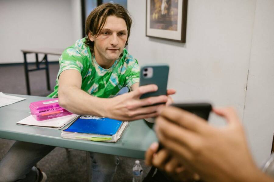 A student sharing his phone screen with another in a classroom setting.