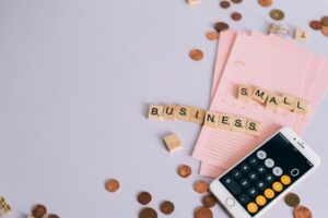網路賺錢成本試算:每月500、1000、3000美元階段目標設定 Flat lay of a small business planning scene with coins, smartphone calculator, and letter tiles.