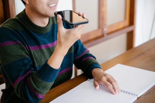 手機語音輸入辨識差怎麼辦:語言包安裝與網路需求指南 Adult man using smartphone for voice commands, smiling at home desk.