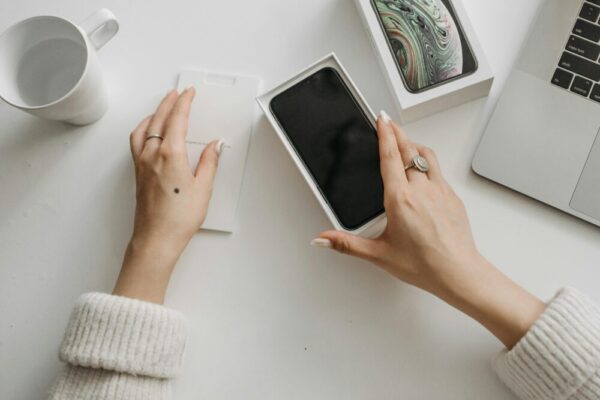 手機產品拍攝指南:小型棚架、補光燈與反光板實用技巧 Woman unboxing a smartphone on a white table, showcasing technology and lifestyle