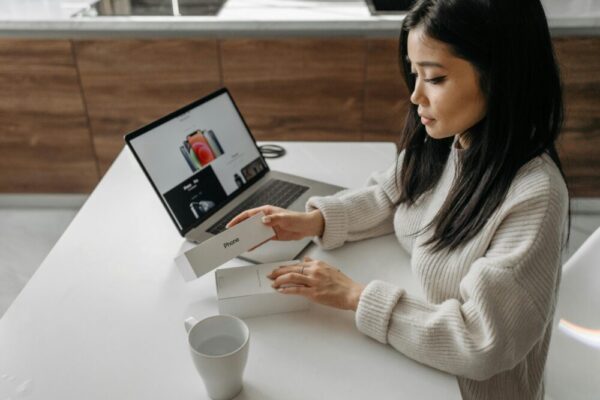 手機開箱影片腳本模板:鏡位與剪接節點指南 Adult woman unboxing a smartphone with a laptop nearby, showcasing technology lifestyle.