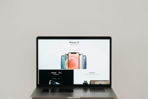 Laptop on stool showing sleek iPhone 12 ad, white background.