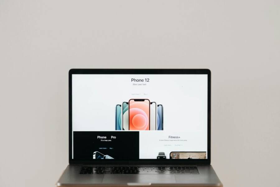 Laptop on stool showing sleek iPhone 12 ad, white background.