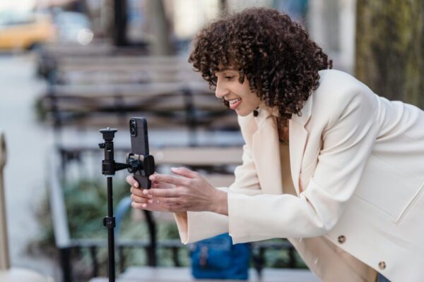 手機錄影教學影片SOP:畫面錄製、投影片與畫中畫實作指南 Cheerful woman setting up smartphone on tripod outdoors for video recording.