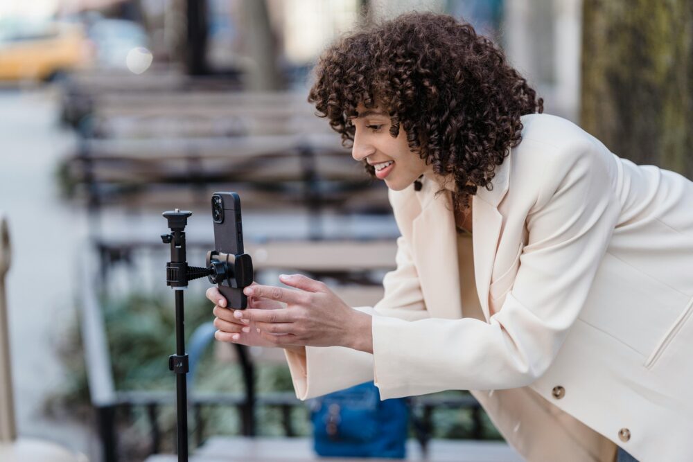 Cheerful woman setting up smartphone on tripod outdoors for video recording.