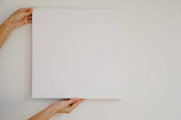 Unrecognizable female demonstrating empty poster of square shape during advertisement campaign against gray wall
