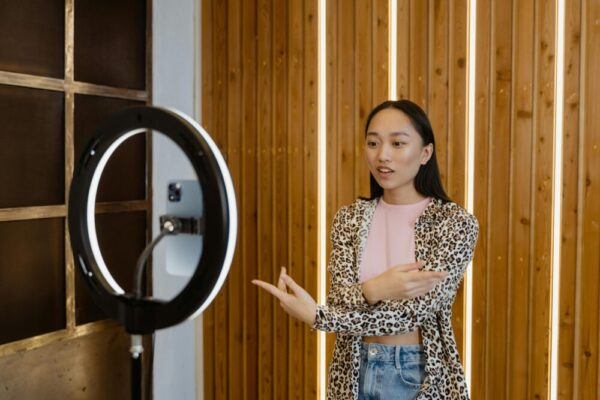Young Asian woman recording a vlog with a ring light indoors, wearing leopard print.