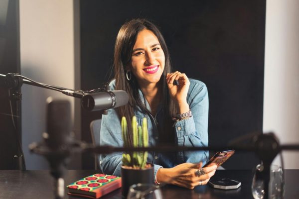 手機錄音筆 App 異常關閉:背景權限設定全攻略 Smiling woman in denim recording a podcast with microphone, phone, and cactus on table.