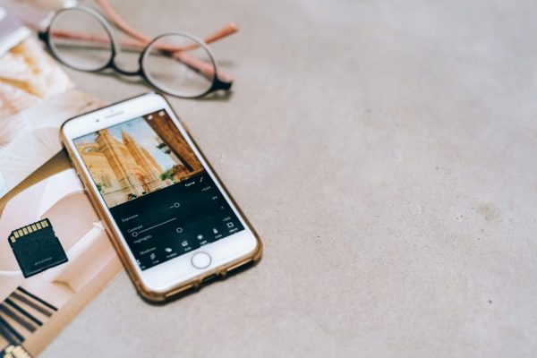 Google 相簿空間不足,手機釋放空間10招(含15GB清理教學) Smartphone displaying a photo editing app, next to a memory card and glasses on a table.