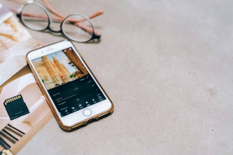 Smartphone displaying a photo editing app, next to a memory card and glasses on a table.