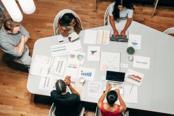 漏斗設計比廣告更重要:行銷漏斗拉高轉換率、降低成本 A diverse group working on marketing strategies with charts and laptops in an office setting.