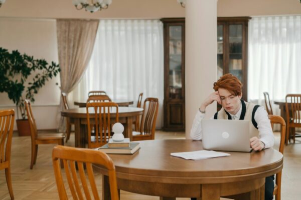 A young man focuses on studying with a laptop in a quiet library environment.