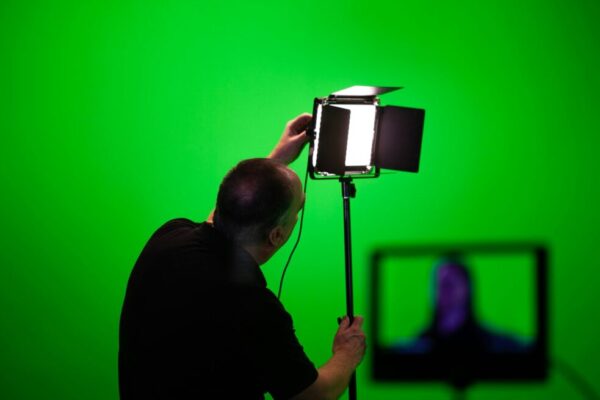 商品拍照指南:簡單技巧讓照片更有質感 Man adjusting lighting equipment in a green screen studio setup.
