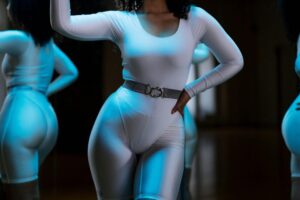 健身修復身體意象:轉化負面自我對話的實用指南 Woman in white leotard posing confidently in front of gym mirror, showcasing fitness and style.