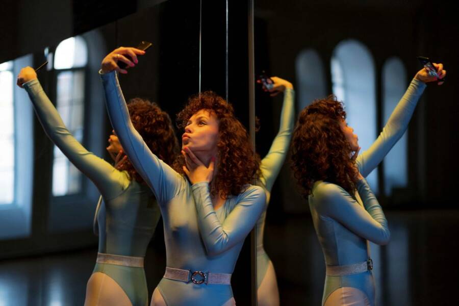Young woman in leotard takes a selfie with reflection in a dimly lit room, showcasing a modern indoor setting.