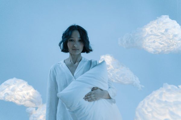 Conceptual image of a woman holding a pillow with floating clouds around her.