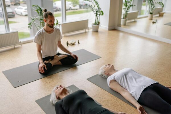 A yoga instructor guides adults in relaxation poses during a class in a bright studio.