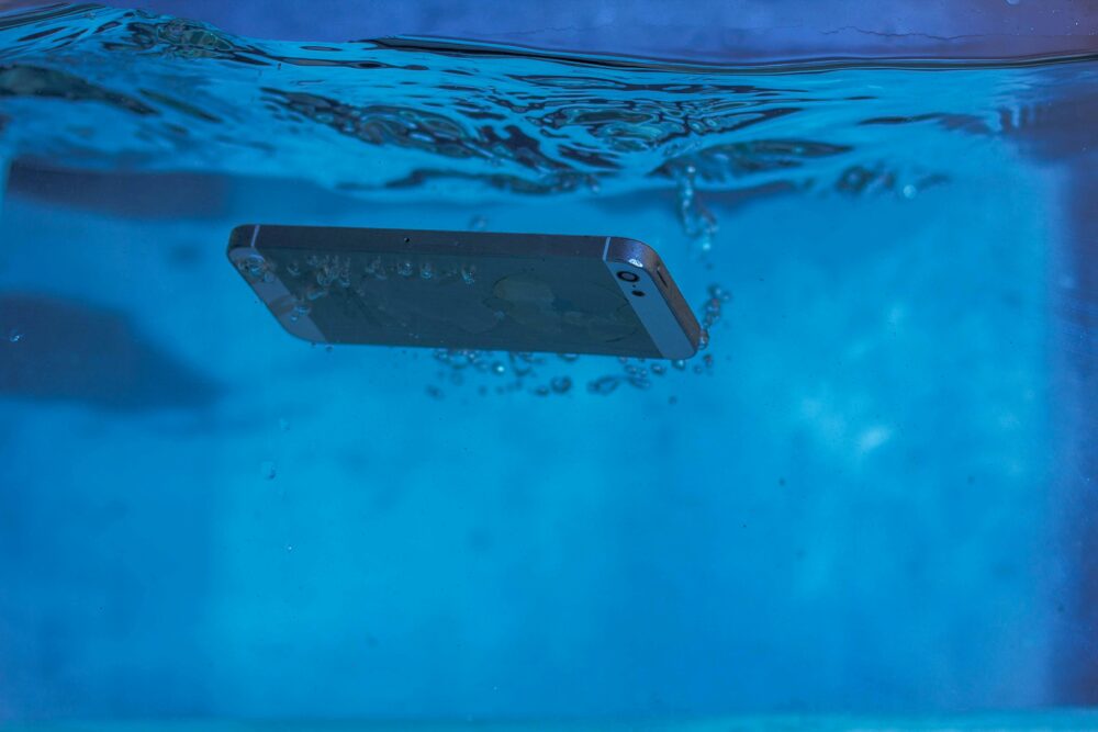 A smartphone underwater displaying air bubbles and motion in vivid blue water.