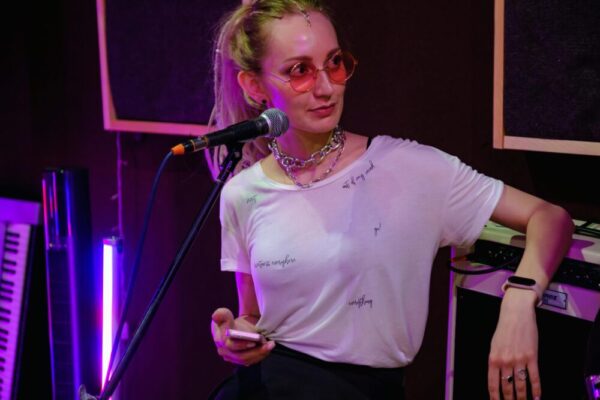 手機外接麥克風選購指南:Type‑C、Lightning 與 3.5mm 的實用要點與差異分析 A woman musician in a studio holding a microphone and smartphone, wearing sunglasses and a chain necklace.