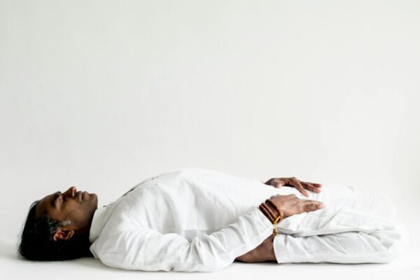 A person in a white outfit practicing meditation, lying down peacefully indoors.