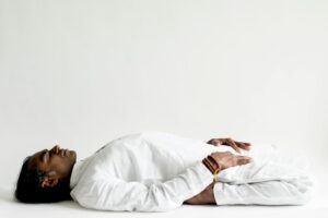 A person in a white outfit practicing meditation, lying down peacefully indoors.