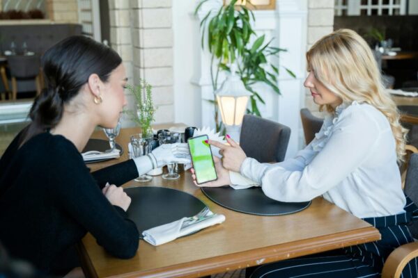 Two women sitting at a café table using a smartphone, one has a prosthetic hand.