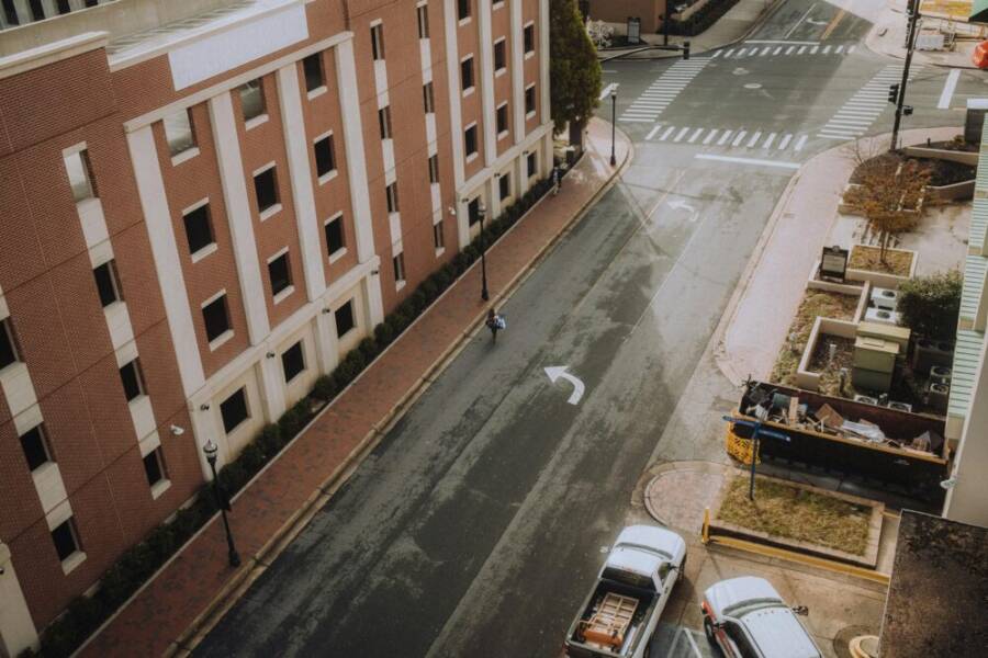 從空中拍攝的空曠城市街道，街道兩旁是磚砌建築，鏡頭中捕捉到一個孤獨的行人。