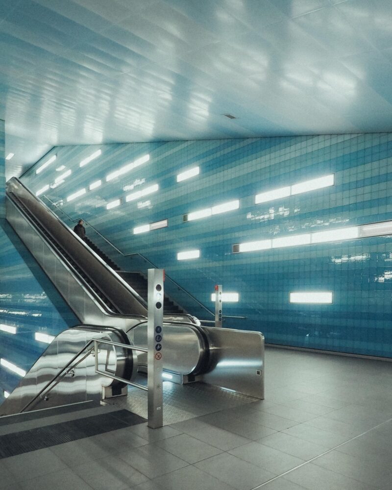 未來感填充的地鐵環境中，一條線條流暢、現代感填充的自動扶梯，牆壁鋪著藍色瓷磚。