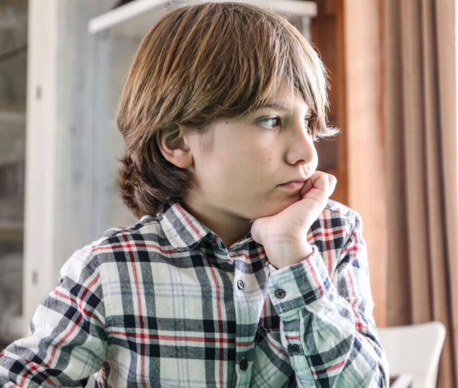 白天，一個穿著格子襯衫的小男孩在室內陷入沉思。