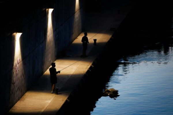 黃昏時分，兩名男子在華沙河邊一條燈光明亮的小路上釣魚。