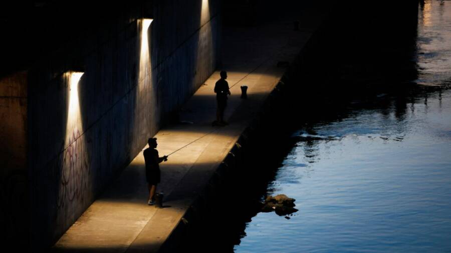黃昏時分，兩名男子在華沙河邊一條燈光明亮的小路上釣魚。