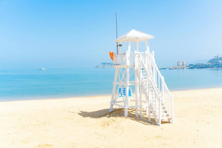 寧靜的海灘景色，有白色的救生塔、清澈的海水和藍天。