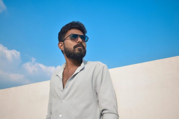 一位男士男士太陽眼鏡，在戶外以湛藍的天空為背景擺姿勢拍照。