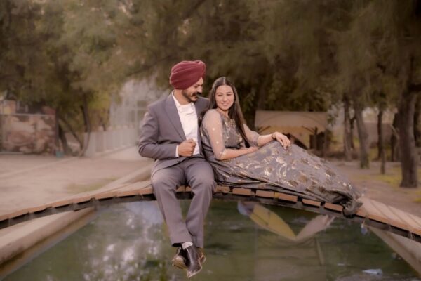 一對身著優雅服飾的夫婦坐落在森林中寧靜的蓄水池上的一座橋上。