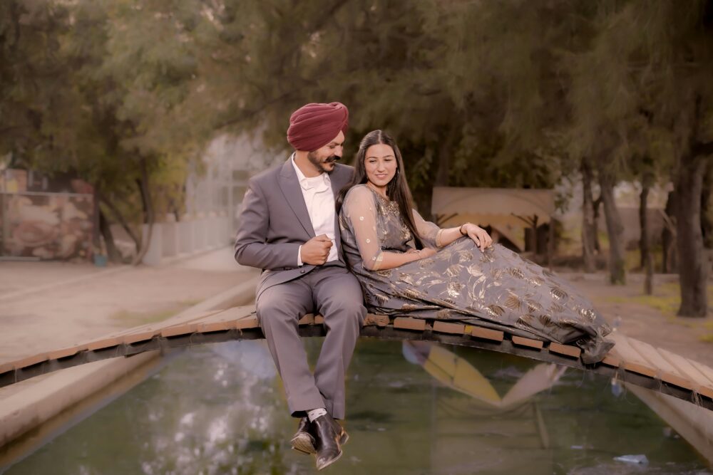 一對身著優雅服飾的夫婦坐落在森林中寧靜的蓄水池上的一座橋上。