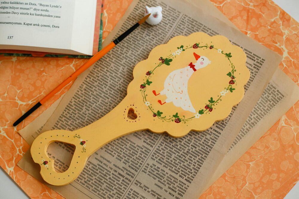 一個造型別緻的木製托盤,上面繪有鴨子圖案,托盤下放著報紙和書籍,旁邊放著畫筆。