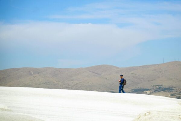 在晴朗的藍色天下，一位徒步旅行者徒步穿越土耳其卡帕多西亞獨特的白色景觀。