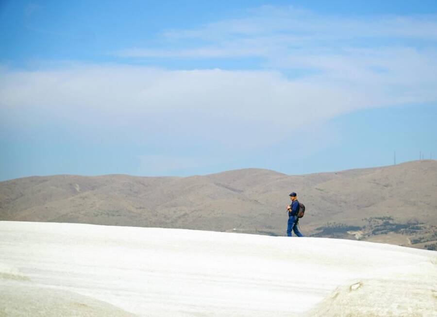 在晴朗的藍色天下，一位徒步旅行者徒步穿越土耳其卡帕多西亞獨特的白色景觀。