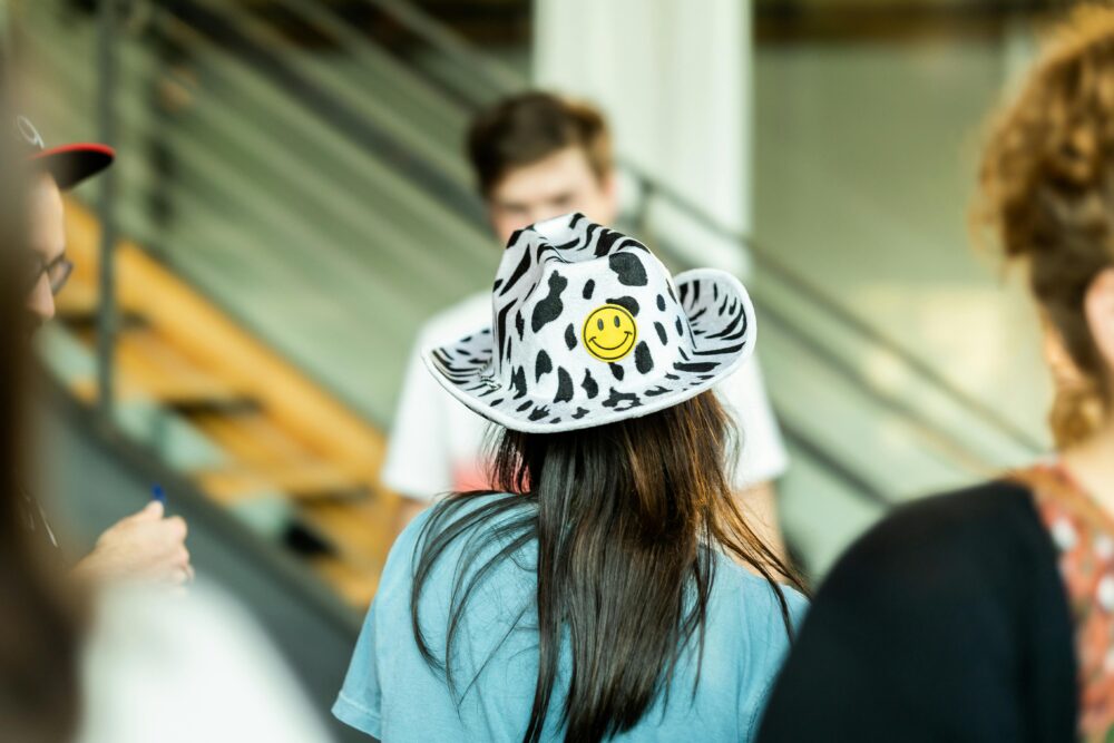 一群人聚集在室內，其中一人戴著一頂獨特的笑臉帽。