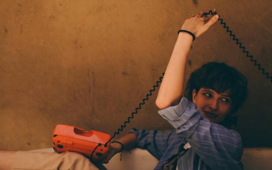 一位年輕女子手持復古橙色轉盤電話的藝術肖像。