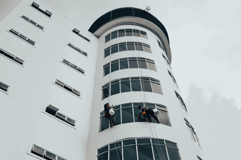 工人們正在使用繩索清潔現代高層建築的窗戶。城市建築維護。