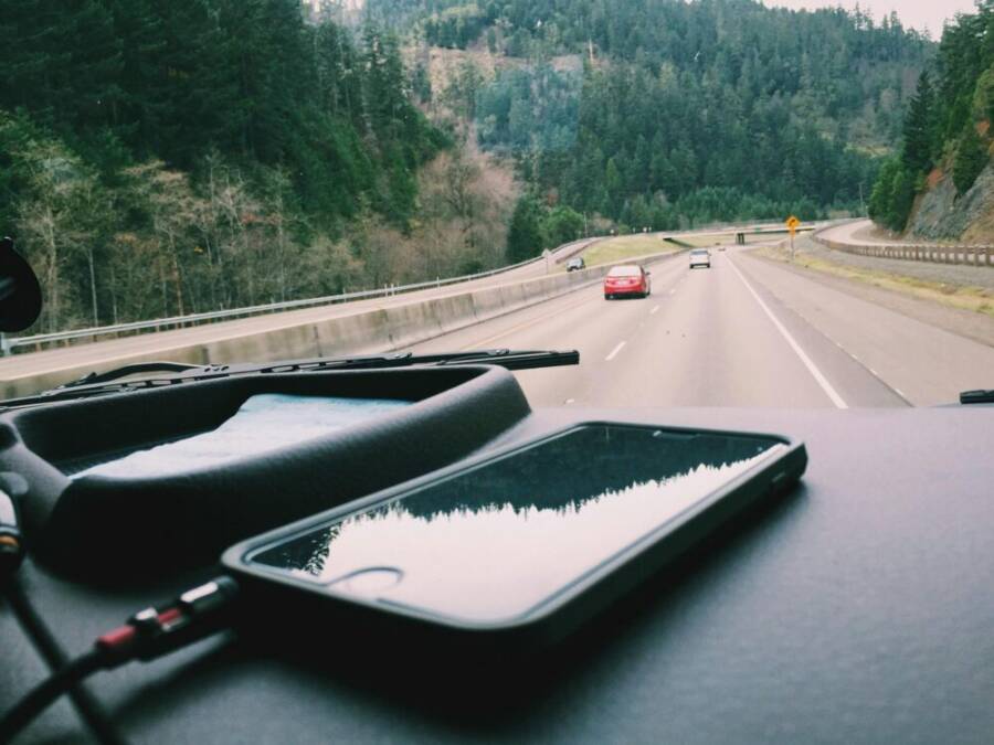 A smartphone charging on the dashboard during a road trip
