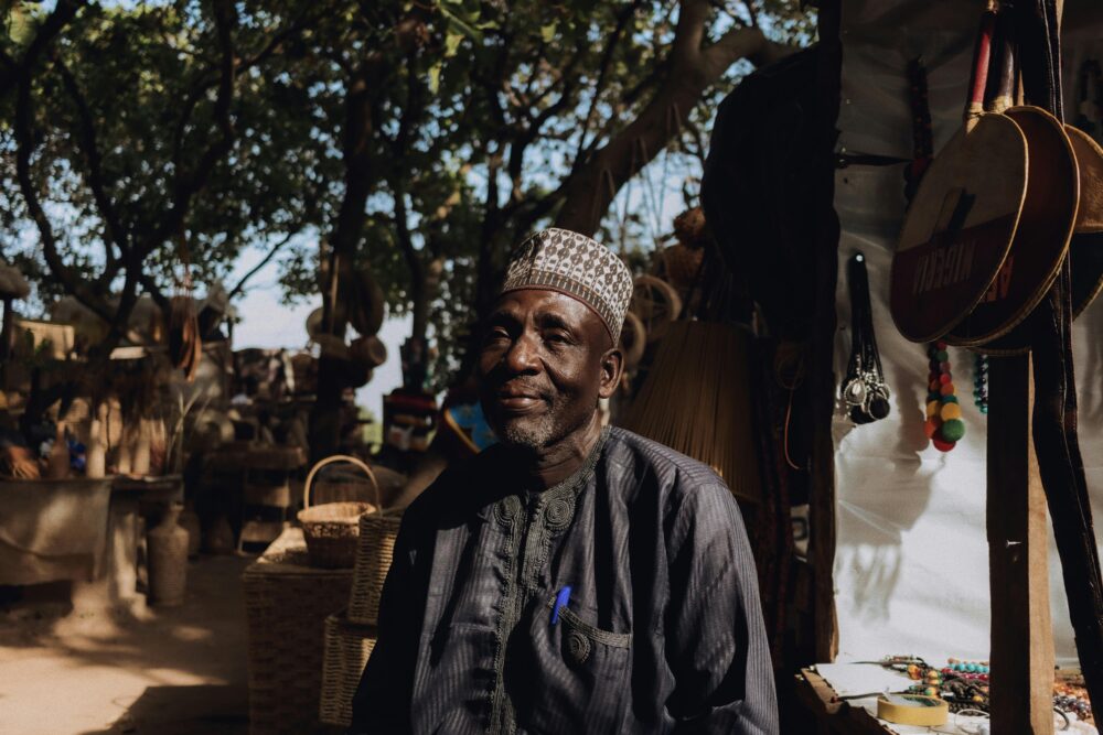 在溫暖的陽光下，尼日利亞市場上的一位老人被傳統工藝品和藝術品包圍著。