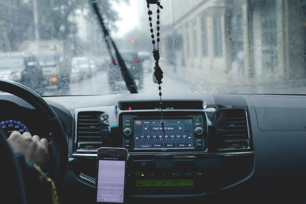 Car interior with driver navigating rainy cityscape using phone and dashboard