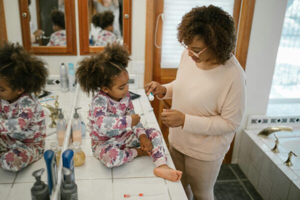 A parent helps a child brush teeth in a bathroom during a morning routine